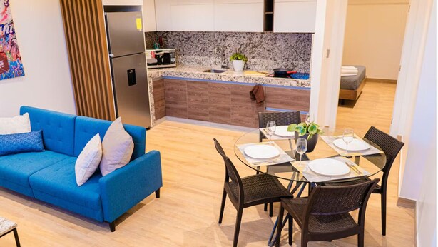 A modern living room with a blue sofa, a dining table set for four, and a kitchen in the background. - 07 Luxury Apartment Los Angeles style, brand new (Guayaquil)
