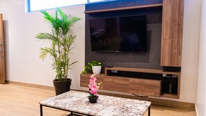 A modern living room with a flat-screen TV mounted on a dark wall, wooden cabinets below, and a marble coffee table with a potted plant. - 07 Luxury Apartment Los Angeles style, brand new (Guayaquil)
