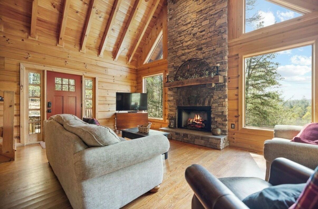 A log cabin interior with a stone fireplace, wooden walls, a sofa, and a television.