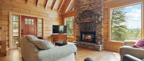 Een blokhutinterieur met een stenen open haard, houten wanden, een bank en een televisie.