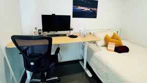 A hotel room with a desk, chair, bed, and a night scene painting.