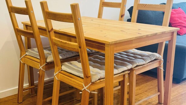 A wooden dining table with four chairs, each with a cushion.