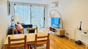 A living room with a dining table, chairs, a sofa, a TV, and a ceiling fan.