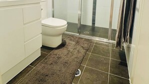 A modern bathroom with a glass-enclosed shower, a white toilet, and a sink with toiletries.