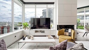 Una sala de estar moderna con televisor grande, asientos cómodos, chimenea y vistas a la ciudad.
