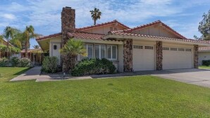 A single-story house with a red-tiled roof, a stone chimney, and a garage. - Charming 3-bedroom house in the heart of Palm Desert! (Palm Desert)