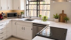A modern kitchen with white cabinetry, a built-in microwave, a toaster, a sink, and a large window with a view of trees. - Charming 3-bedroom house in the heart of Palm Desert! (Palm Desert)
