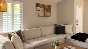 A living room with a beige sectional sofa, a wooden coffee table, and a door. - Charming 3-bedroom house in the heart of Palm Desert! (Palm Desert)