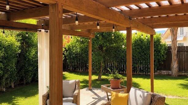 A covered patio area with wicker furniture, a round table, and a potted plant. - Charming 3-bedroom house in the heart of Palm Desert! (Palm Desert)