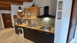 A compact kitchen with a stone backsplash, wooden shelves, a built-in oven, and a sink. - Nautilus - Cozy Apartment with Terrace in the City Center (Cagliari)