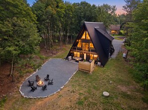 Une cabane moderne de forme triangulaire, dotée d’un foyer et d’un espace salon extérieur.