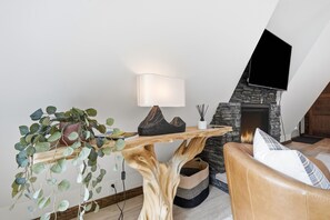 Ein modernes Wohnzimmer mit Kamin aus Stein, einem wandmontierten Fernseher, einem Holztisch und einer Ledersofa.