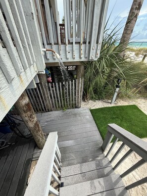 Eine Holzterrasse führt zu einem Strandhaus mit einem kleinen Rasen und Blick auf den Ozean.
