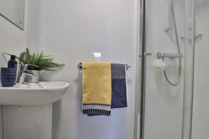 A bathroom with a sink, a towel rack with a yellow and blue towel, a potted plant, and a shower area. - Student Only Percys Place (York)