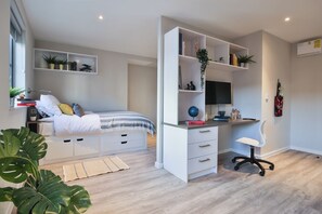 Ein Schlafzimmer mit Bett, Nachttischen, einem Schreibtisch mit Stuhl, Regalen mit Pflanzen und einem Fernseher.