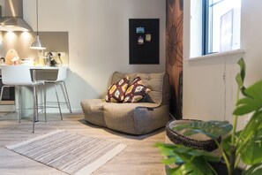 Ein modernes Wohnzimmer mit einer Couch, einem Essbereich mit weißem Tisch und Stühlen, einer hängenden Pendelleuchte und einem gerahmten Bild an der Wand.