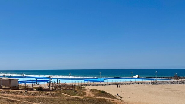 Ein Strand mit blauem Himmel, sandigem Ufer und einem Poolbereich.