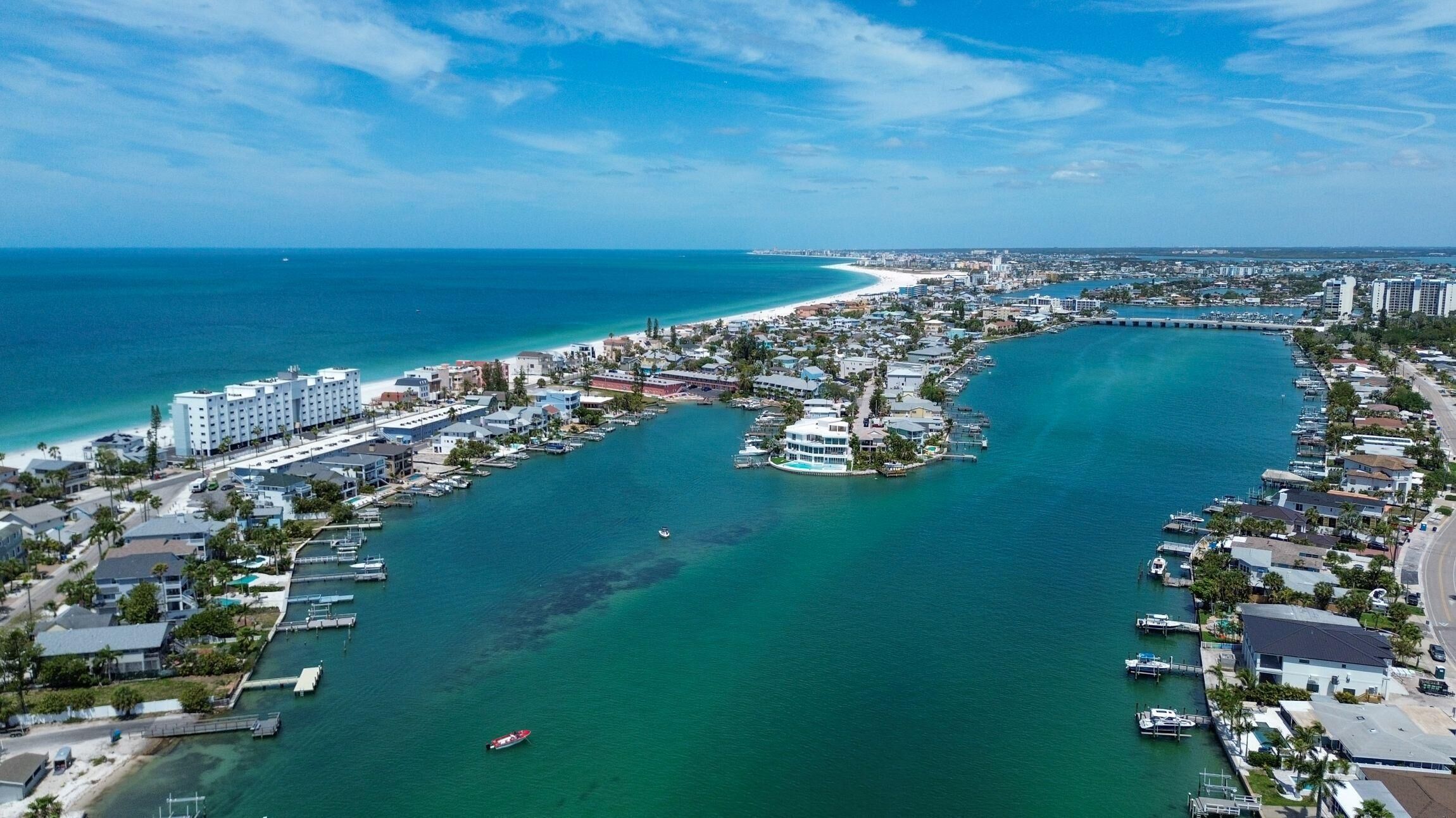 An aerial view of a coastal town with a marina, buildings, and a beach.