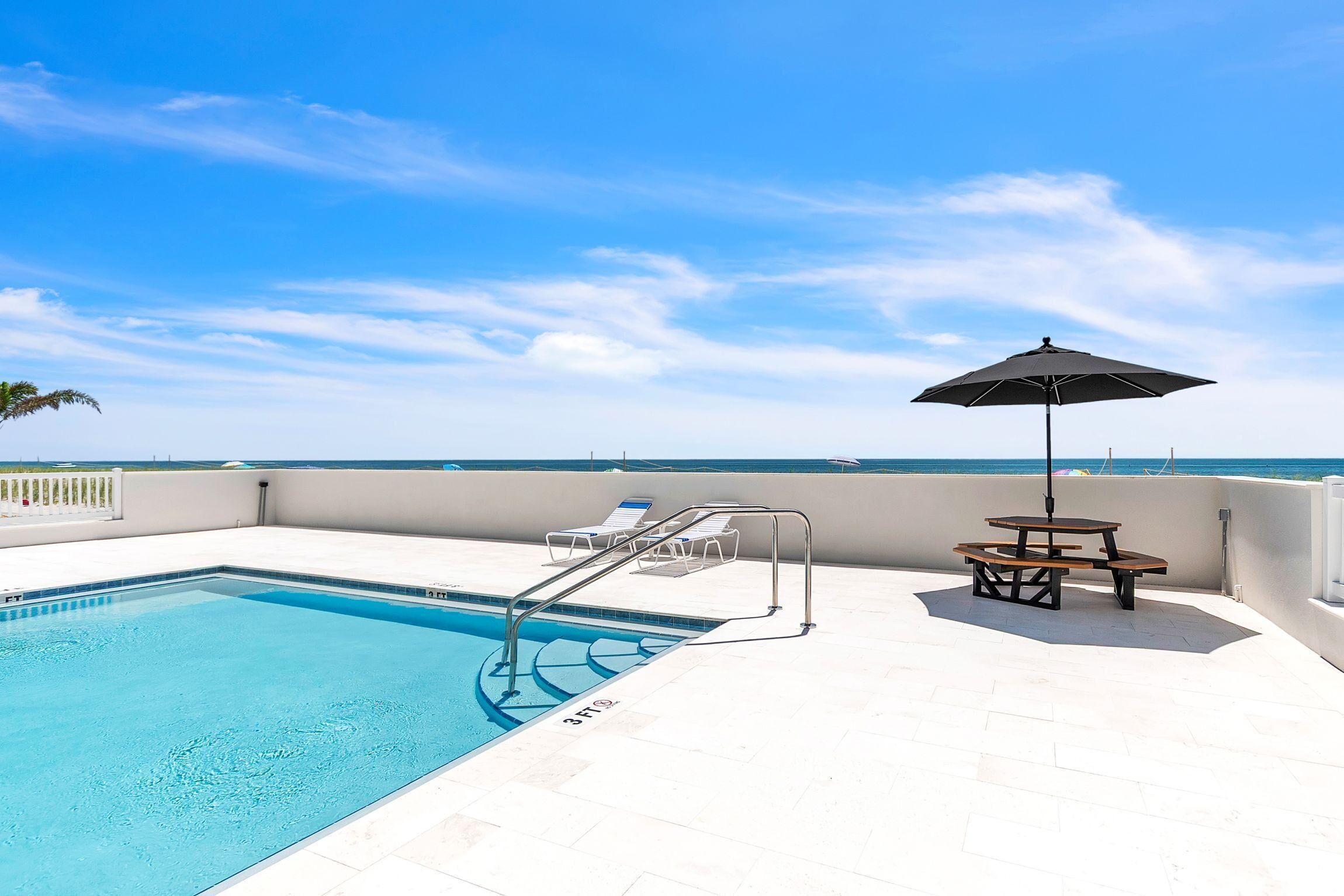 A swimming pool with a sun umbrella, lounge chairs, and a view of the ocean.