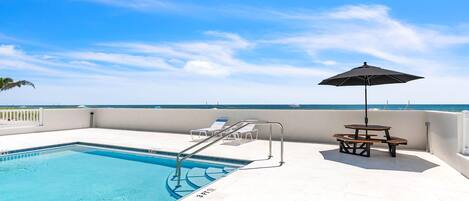 Une piscine avec un parasol, des chaises longues et une vue sur l’océan.