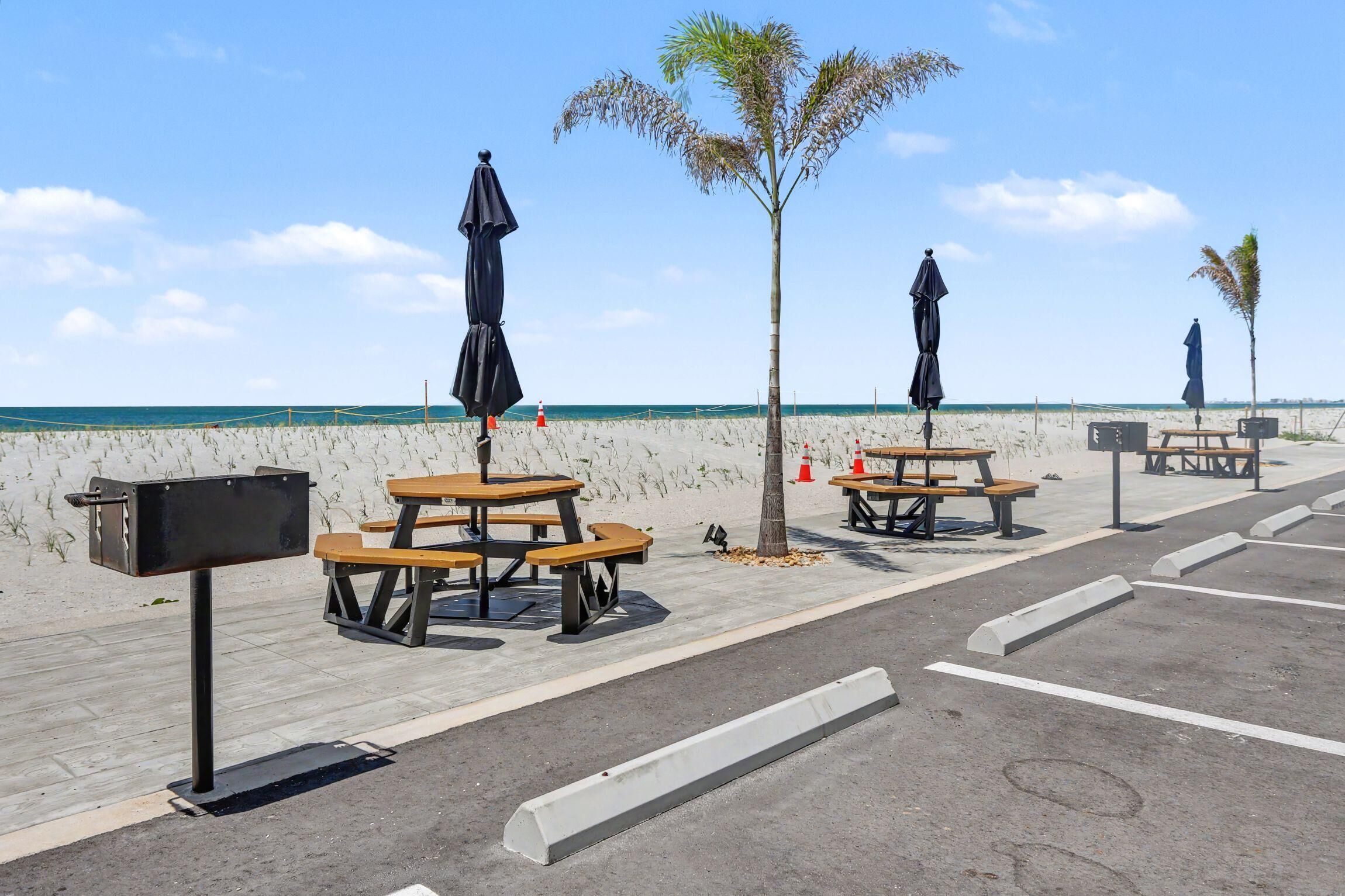 Un espace de pique-nique aménagé sur la plage, avec des tables, des bancs, des parasols et une boîte aux lettres.