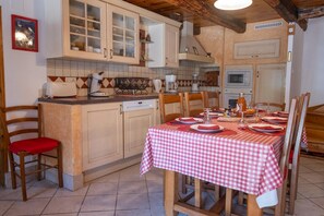 A kitchen with wooden cabinets, a dining table set for four, and a checkered tablecloth. - Au Pied de l'Aubrac - SALCES (LES) (SALCES (LES))