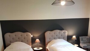 A room with two beds, a hanging light fixture, a round table, and a chair. - GÎTE GABRIELLE - BAGNOLS-LES-BAINS (BAGNOLS-LES-BAINS)