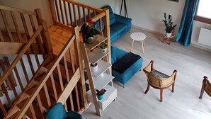 A room with a wooden staircase, blue sofa, wicker chairs, a small table, and a floor lamp. - GÎTE GABRIELLE - BAGNOLS-LES-BAINS (BAGNOLS-LES-BAINS)