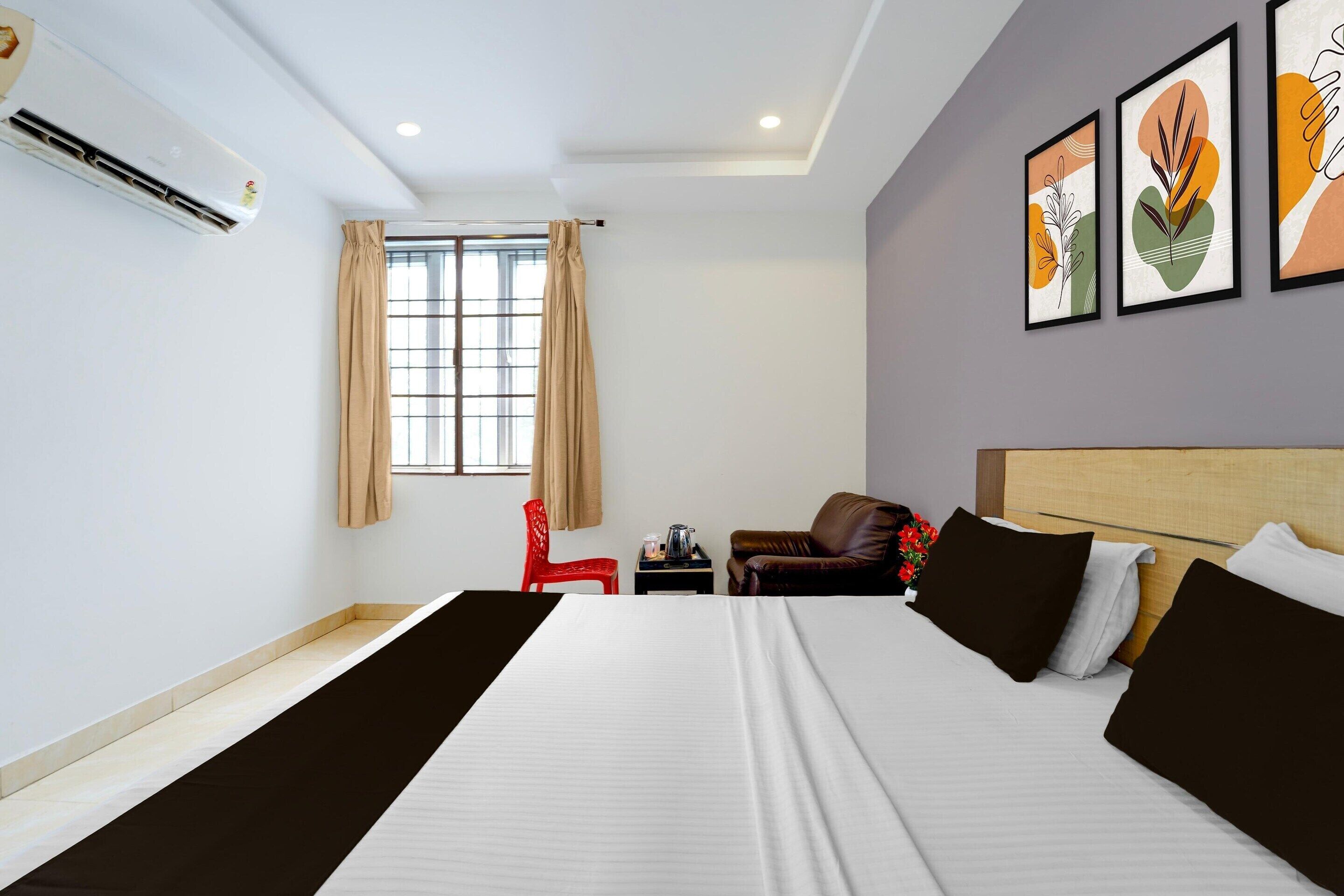 A hotel room with a bed, a red chair, a small table, and artwork on the wall.