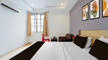 A hotel room with a bed, a red chair, a small table, and artwork on the wall.