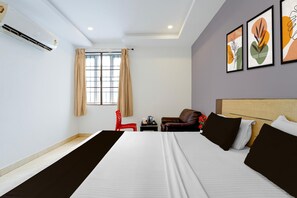 Una habitación de hotel con una cama, una silla roja, una mesita y obras de arte en la pared.