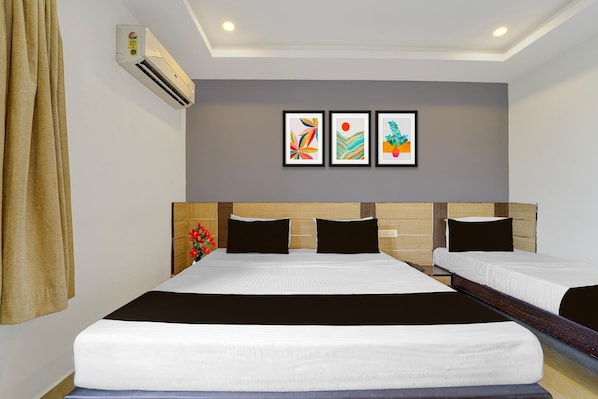 A hotel room with two beds, a headboard with a wooden panel, a wall-mounted air conditioner, and three framed artworks.