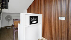 Una habitación con pared de paneles de madera, un armario blanco con un letrero, una silla y un ventilador de pie.