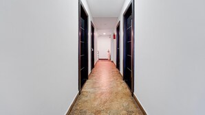 Un pasillo largo y estrecho con puertas a ambos lados, suelo de baldosas y una lámpara en el techo.