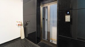 Un ascensor con detalles metálicos, un teléfono de emergencia en la pared y un jarrón con flores en el suelo.
