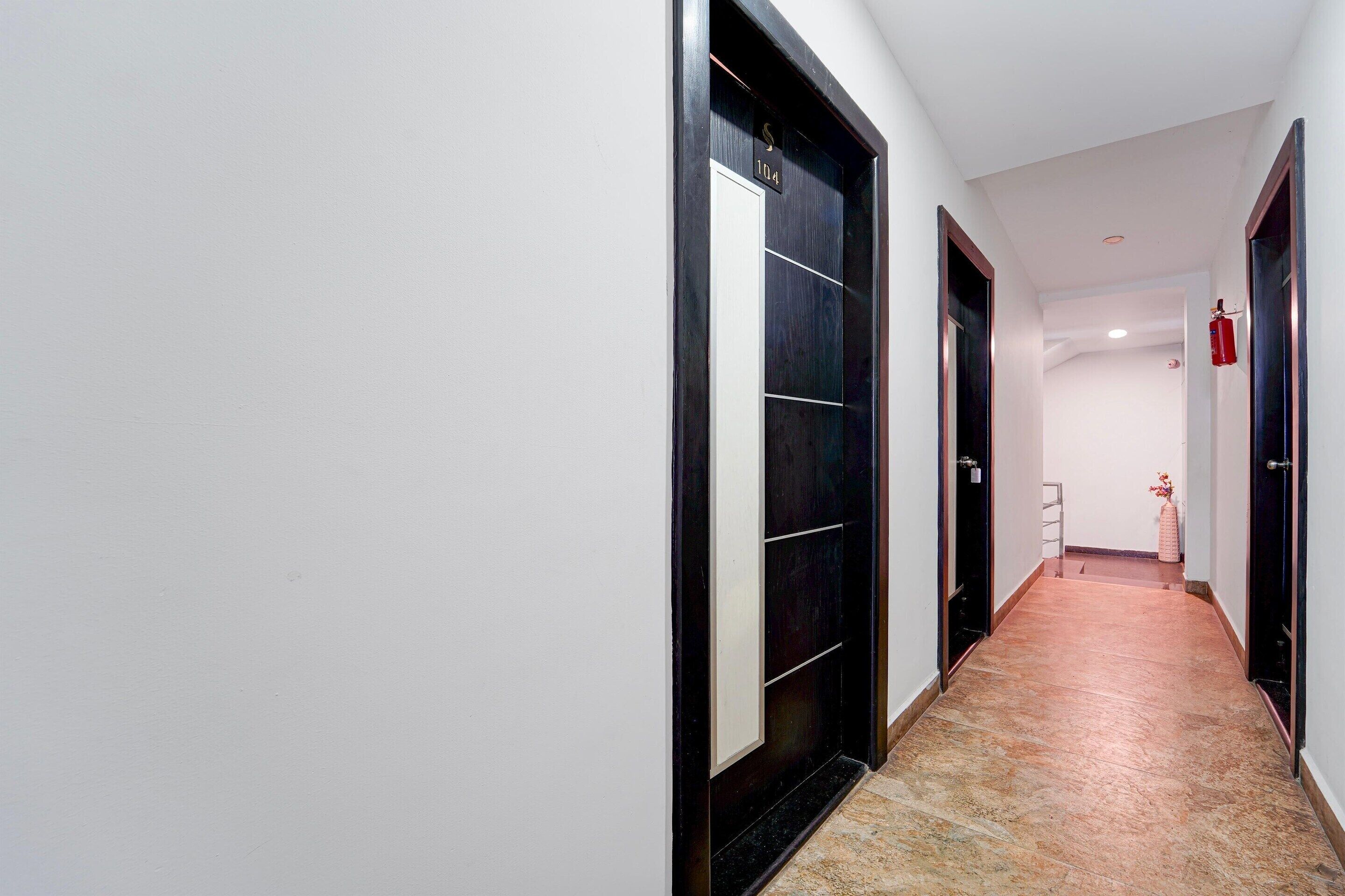 A hallway with a black door, a white wall, and a tiled floor.