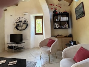 Ein Wohnzimmer mit Fernseher, zwei weiße Stühle mit roten Kissen, einem Bücherregal und einer runden Wanddekoration.