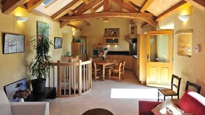 A spacious living area with a high ceiling, wooden beams, a dining table, and a kitchen in the background. - Gîte de Poussiels - SAINT ANDEOL DE CLERGUEMORT (SAINT ANDEOL DE CLERGUEMORT)