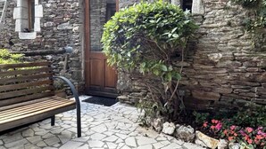 A stone building with a wooden door, a bench, and a small garden with pink flowers. - Gîte de Poussiels - SAINT ANDEOL DE CLERGUEMORT (SAINT ANDEOL DE CLERGUEMORT)
