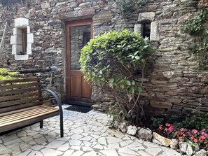 Ein Steinhaus mit einer Holztür, einer Bank und einem kleinen Garten mit rosa Blumen.
