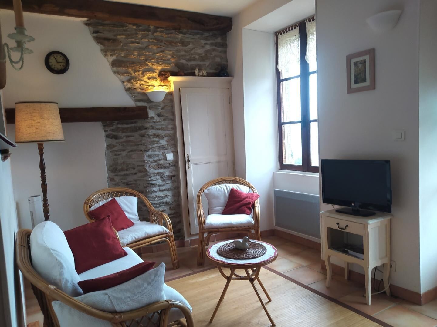 Un salon avec des meubles en osier, un téléviseur, un mur en pierre et une fenêtre.