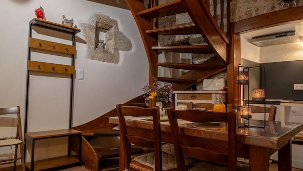 A wooden staircase leading to a loft bedroom with a stone wall, a dining area with chairs and a table, and a kitchen area with a stove and cabinets. - Gîte de la Volte in Sainte Enimie (SAINTE-ENIMIE)