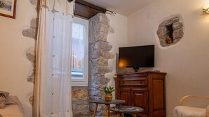 A cozy room with a stone wall, a television, a wooden cabinet, a small table with a plant, and a chair. - Gîte de la Volte in Sainte Enimie (SAINTE-ENIMIE)