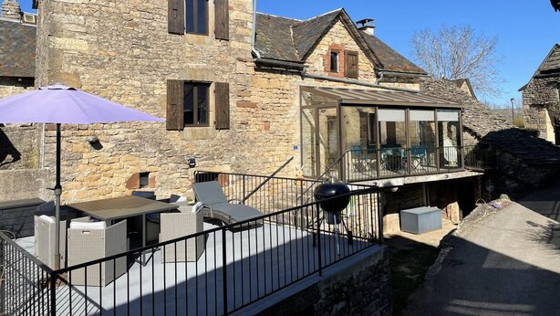 Ein Steinhaus mit Glasanbau, Außenbereich mit Sitzgelegenheiten und einem Grill.