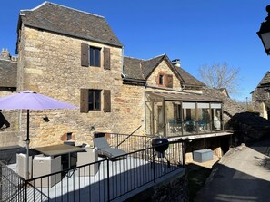 A stone building with a glass extension, outdoor seating, and a barbecue grill. - Le Gîte du Donjon - CANILHAC (CANILHAC)