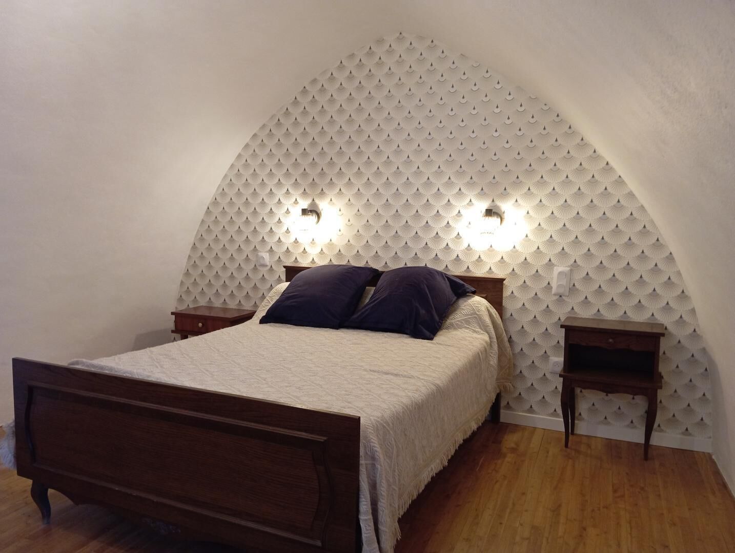 A bedroom with a bed, two bedside tables, and a unique ceiling design.