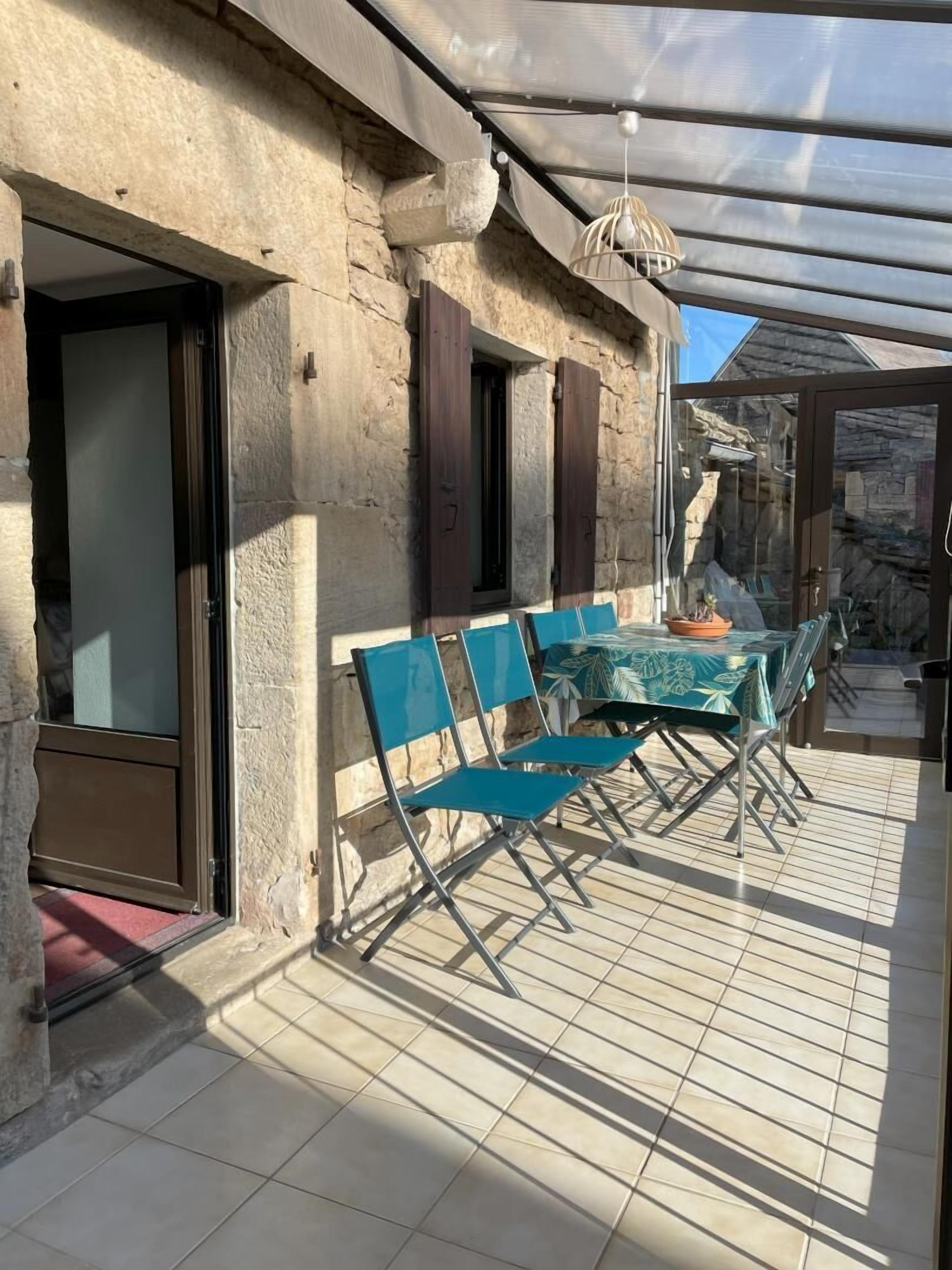 Een overdekt terras met een tafel en stoelen, stenen muren en een glazen deur.