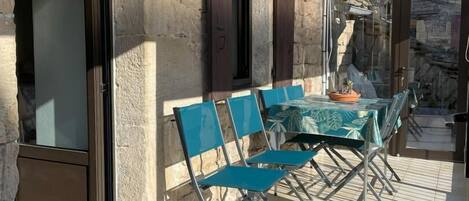 Een overdekt terras met een tafel en stoelen, stenen muren en een glazen deur.
