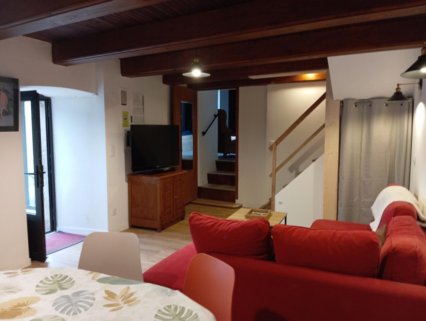A living room with a red sofa, a television on a wooden cabinet, and a staircase leading to another room.