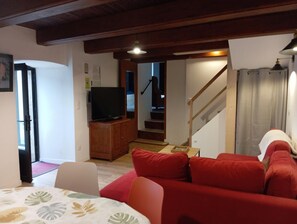 Ein Wohnzimmer mit einem roten Sofa, einem Fernseher auf einer Holzkommode und einer Treppe, die in einen anderen Raum führt.